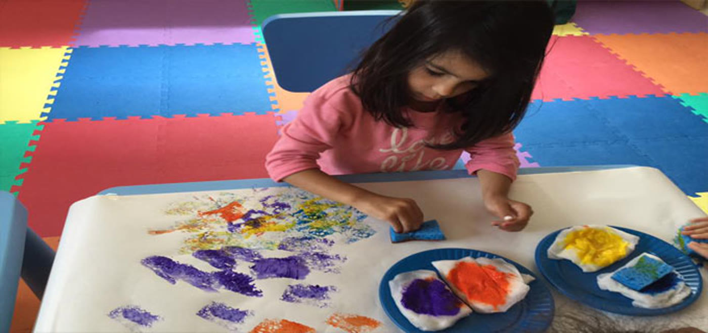 A child at Little Bird Child Care stamping paint shapes onto paper during an art activity